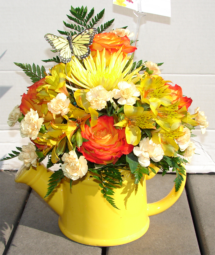Assorted bright flowers in a yellow watering pot